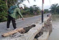Seorang warga melintas menunjuk ke arah bangunan gorong gorong yang berlubang. (Foto/Edi)