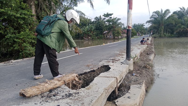 Seorang warga melintas menunjuk ke arah bangunan gorong gorong yang berlubang. (Foto/Edi)